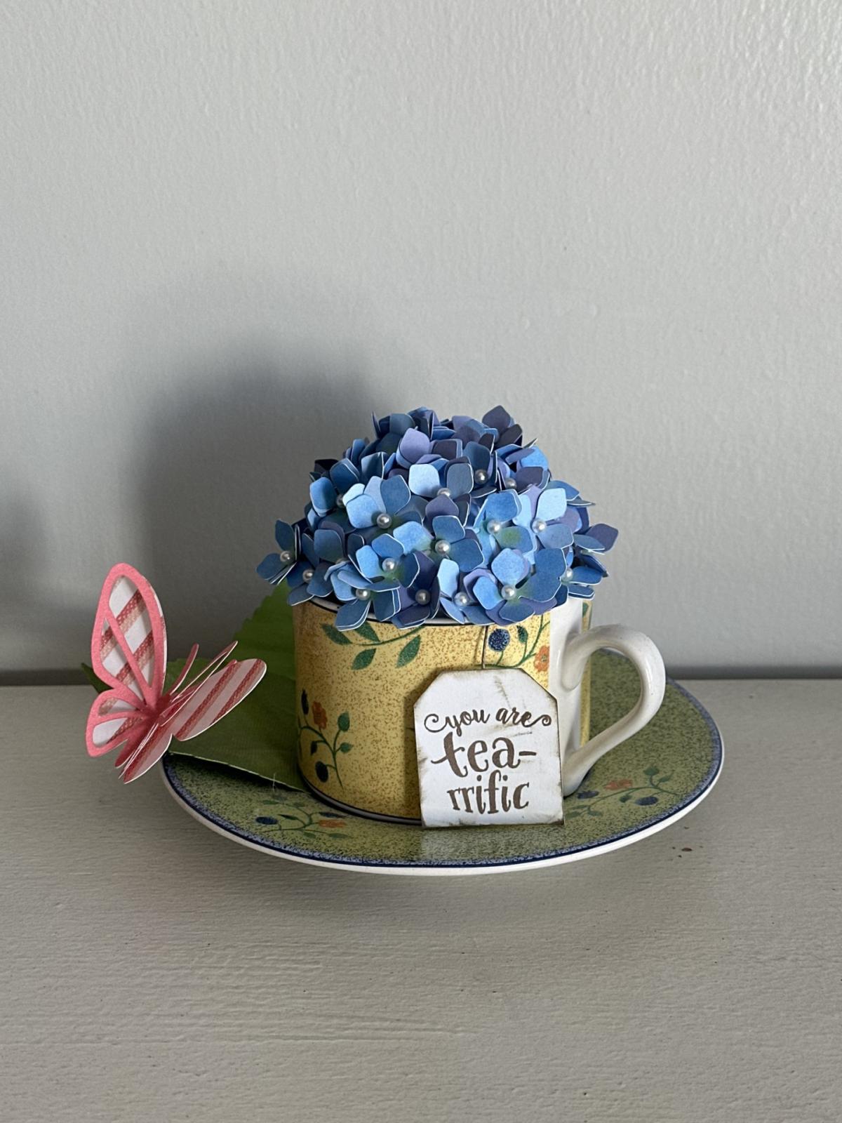 Blue hydrangea flowers in yellow tea cup on green plate