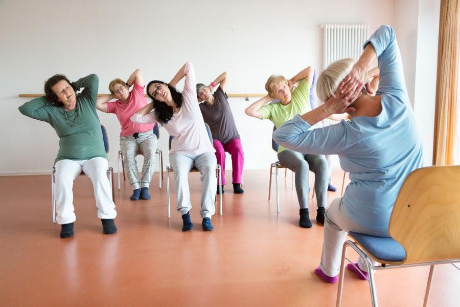 patrons in chairs doing a yoga stretch